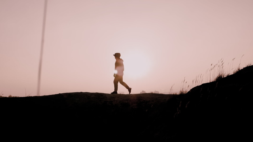 Silhouette of a walking man at sunset on the top of the mountain. The winner who crossed the top | Shutterstock HD Video #1082033825