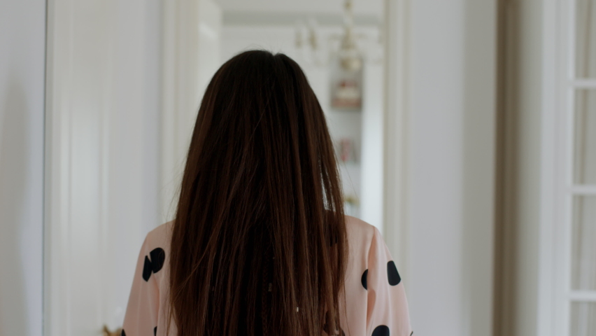 a woman with cute pyjamas shorts and too stretches out her arms high in the air while she walks away into a different room