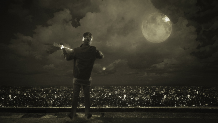 Moonlight Serenade Musician Playing Guitar Over City at Night. Male musician playing acoustic guitar under moonlight on top of a building with city view at night
