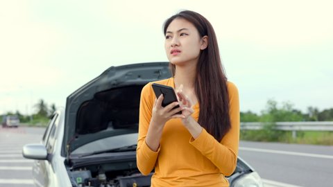 Young asian woman has broken down car on the road she feeling serious and stressed. Look for someone help. Using smartphone Call Emergency assistance or insurance service.