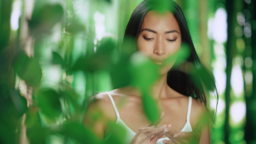 Portrait of Beautiful Asian Woman Gently Applying Face Cream. Young Adult Female Makes Her Skin Soft, Smooth Using Scientifically Advanced Natural Cosmetics Skincare Product. Green Forest Background Royalty-Free Stock Footage #1082039750