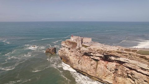 Aerial flying over clifftop Saint Michael the Archangel fort and Nazare lighthouse with beautiful seascape.