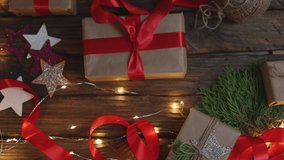 female woman hands wrapping Christmas presents gift box with brown craft paper, tying red ribbon bow on wooden desk with new year ornaments: stars light garland and green coniferous. top view DIY home - Powered by Shutterstock - Get 15% off with code: PIKWIZARD15