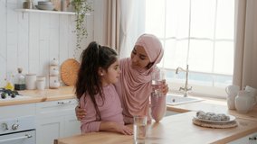 Healthy Hydration. Happy Muslim Mother In Hijab And Little Daughter Drinking Water From Glasses Sitting In Modern Kitchen Indoors. Stay Hydrated, Family Nutrition Concept. Slowmo