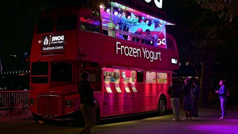 LONDON - SEPTEMBER 14, 2021: Customers at a Red Double Decker bus converted into a frozen yoghurt cafe on London's Southbank at night.