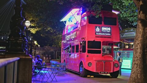 LONDON - SEPTEMBER 14, 2021: Nighttime diners at a Red Double Decker bus converted into a frozen yoghurt cafe on London's Southbank.