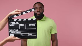 Young african american man 20s wears green t-shirt after black film making clapperboard play act cry shout scream why look up raise hands isolated on plain pastel light pink background studio portrait