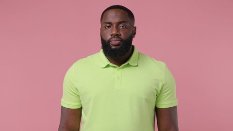 Puzzled gloomy young bearded african american man 20s wears green t-shirt look aside put hand prop up on chin iterates over solution options isolated plain pastel light pink background studio portrait