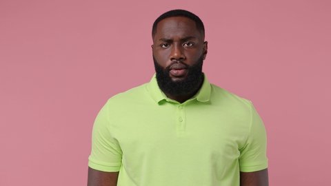 Secret wistful young bearded african american man 20s wears green t-shirt look aside say hush be quiet with finger on lips shhh gesture isolated on plain pastel light pink background studio portrait