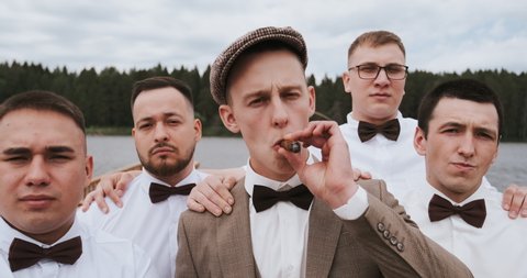 Men's band, group of gangsters friends, cool guys looking at camera. A man boss is smoking cigar, exhales smoke in the camera. Gang of serious men with leader or ringleader.