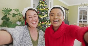 Happy diverse female friends in santa hats making christmas video call, blowing kisses and smiling. christmas, festivity and communication technology.