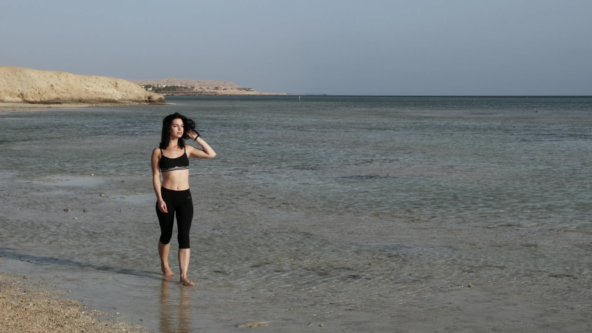 Attractive young woman sportsman walking along the seaside and enjoying vacation. Summer time concept