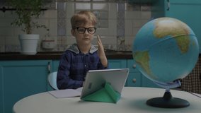 6 years old school boy studying online using tablet computer from home. Kid in eye glasses has online school class sitting at kitchen. - Powered by Shutterstock - Get 15% off with code: PIKWIZARD15