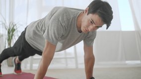 Muscular Man Doing Fitness and Working Out on a Mat. Athlete With Lots of Stamina Doing a Plank Exercise Using a Tablet App, Timing in a Stopwatch.