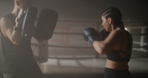 Young Woman Athlete and Caucasian Man Training in Haze on Boxing Ring. Sparring of Young Sportswoman and Personal Trainer in Backlight. Combat Sport, Lifestyle.