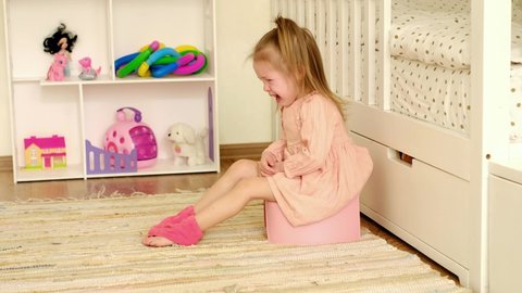 The girl is sitting on a potty in the nursery and crying bitterly. Attempts to teach the child to the toilet. Crying, tears and childish tantrums