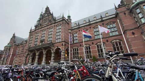 GRONINGEN, NETHERLANDS - 15. OCTOBER 2021: Historical Building of the University of Groningen with Flags waving in the Wind. Bicycles parked in front of the University