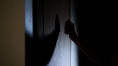 A man knocks on the door with his hand in the dark, an elderly woman knocks on the door