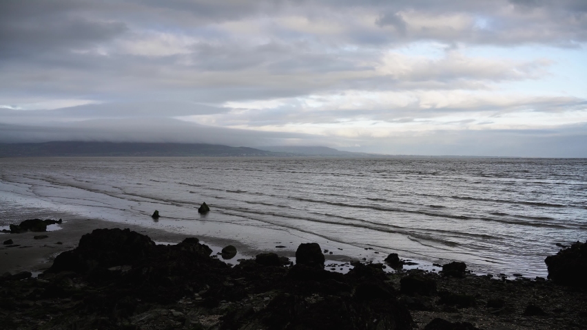 Timelapse of waves crashing on a sandy beach, rocks on the seashore , cloudy weather in Dundalk, Ireland
