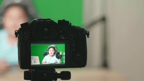 Camera Display Of Asian Little Boy Holding Mobile Phone And Talking To Camera While Live Stream On Green Screen 
