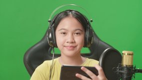 Asian Kid Girl Holding Mobile Phone And Talking To Camera While Live Stream On Green Screen 
