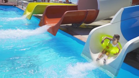 Happy child play in the aqua park, roll down the slide of water pipe. Little Girl dive into the pool of the water park front view. Weekend as a family with kids on water attractions