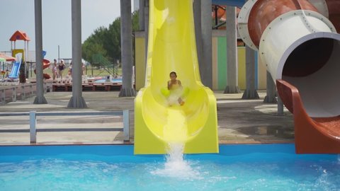 schoolgirl rolls down slide in water park. Summer holidays as a family in the water park. child on an inflatable circle slides along a water slide and dives into the pool