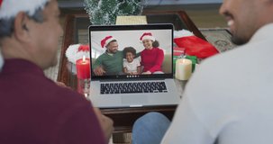 Smiling biracial father and son using laptop for christmas video call with happy family on screen. christmas, festivity and communication technology.