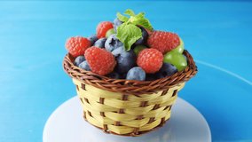 Rotating wooden basket with different forest berries close-up on a blue wooden table. 4k slow motion loop video with speed ramp effect.