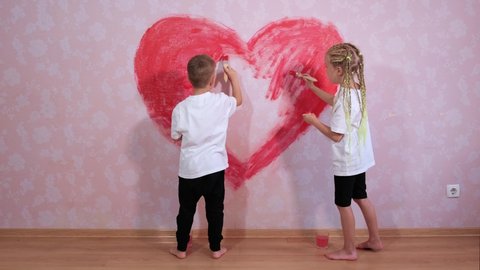 A little girl and a boy paint the red heart of the house on the wall on pink wallpaper. The concept of a happy childhood and children's love.