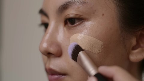 Closeup face, Asian woman using brush applying foundation on her face.