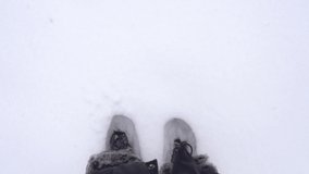 Top view 4k video of two female legs wearing winter boots standing alone in thick fresh white snow covering ground outdoors