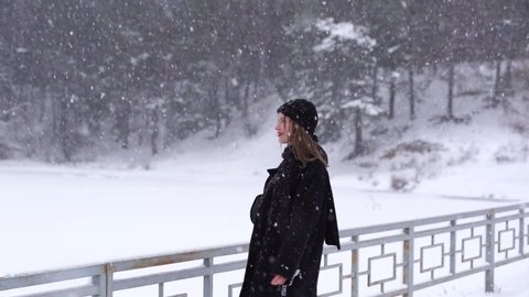 Video footage of beautiful happy attractive european woman enjoying winter snowy weather outdoors in cold white frosty landscape. Video portrait of happy woman walking happily under falling snow