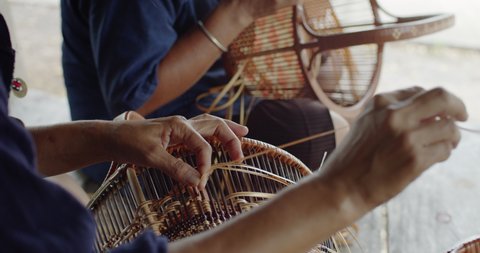 Cut in shot of 2 Thai female farmers weave baskets in traditional Thai art patterns to sell as extra income in countryside of Thailand.
