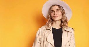 Excited surprised woman look at side, say wow and pointing hands aside isolated on yellow background. Curly blonde girl wear beige trench coat and white hat. Look over here. Sale here!