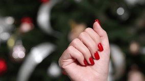 Close-up view 4k stock video footage of one beautiful manicured female hand isolated on blurry holiday festive green Christmas tree background. Woman makes snapping fingers gesture happily