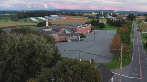 Aerial of exterior, red brick Christian church and steeple in rural America. Cemetery, graveyard and parking lot. Front entrance portico.