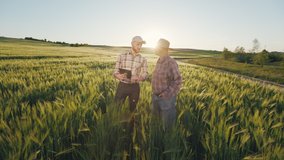 A man is showing an old farmer information on a tablet. They are discussing the harvest. Sunset in the background. The camera is approaching them. 4K - Powered by Shutterstock - Get 15% off with code: PIKWIZARD15