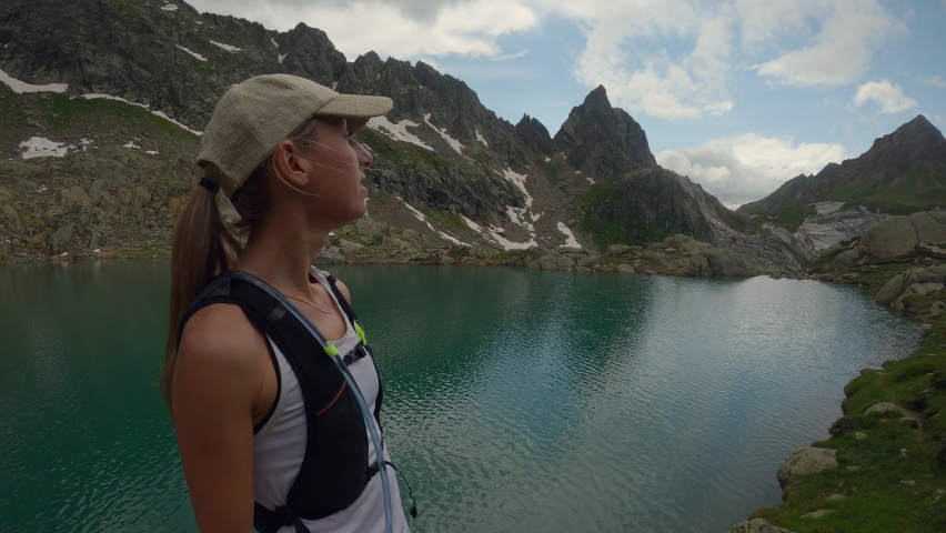 Trail runner stands by a mountain lake arms wide open. Healthy young woman arms wide open in nature 