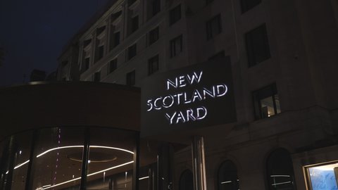 A spinning ‘New Scotland Yard’ sign by a building at night.