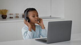 Cute Little Black Boy Wearing Wireless Headphones Listening Music Online On Computer, Cheerful African American Male Child Sitting At Table With Laptop And Enjoying Favorite Song, Slow Motion Footage