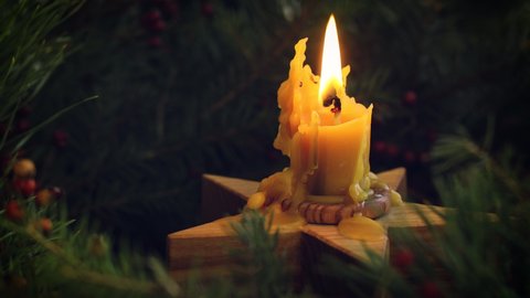 Christmas time. Candle in wooden star candlestick burning in christmas wreath closeup on moody rustic background of fir branches. Merry Christmas! Atmospheric Xmas footage