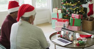 Two senior diverse female friends using laptop for christmas video call with man on screen. christmas, festivity and communication technology.