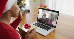 African american woman with santa hat using laptop for christmas video call, with family on screen. christmas, festivity and communication technology during covid 19 pandemic.