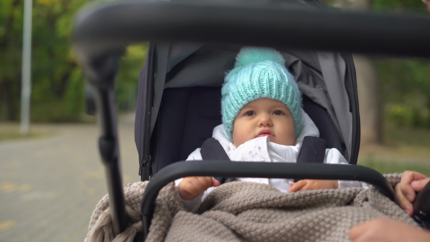 Close-up baby girl sitting in a stroller in the park. Autumn walk with my daughter in a stroller. Happy childhood.