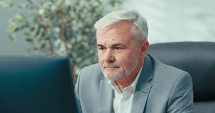 Elegant man in suit with gray hair conducts remote conference from office sitting at desk in front of laptop screen remote greeting chat with colleague online business meetings via webcam, video chat