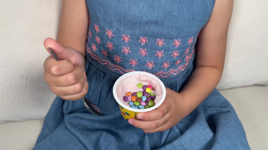 Йогурт - yoghurt. 5 years old girl eating yoghurt with colorful sweets. Little girl in blue dress.