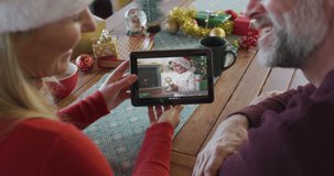 Smiling caucasian couple with santa hats using tablet for christmas video call with boy on screen. christmas, festivity and communication technology.