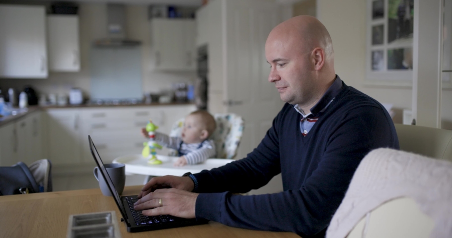 Young father working from home and playing with his newborn baby boy in the living room. Parent and son authentic scene at home with concepts of remote work, children, parenthood, lifestyle in the UK | Shutterstock HD Video #1082129267