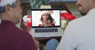 Smiling biracial father and son using laptop for christmas video call with woman on screen. christmas, festivity and communication technology.